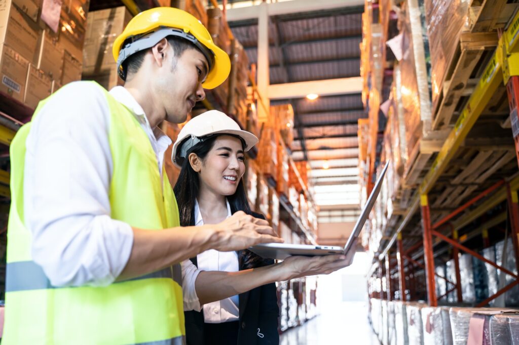 Two Asian workers wear safety helmet working in warehouse.